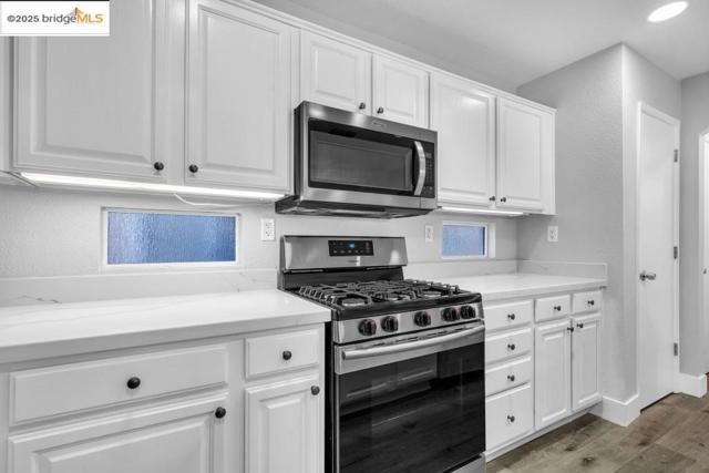 Kitchen with appliances with stainless steel finishes, wood finished floors, white cabinets, and a textured wall