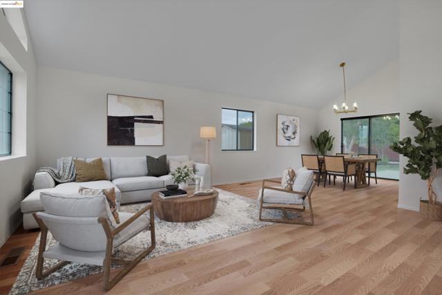 Living area with plenty of natural light, high vaulted ceiling, wood finished floors, and a chandelier