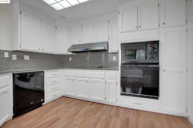 Kitchen with black appliances, backsplash, white cabinets, and light wood finished floors