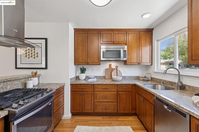 Kitchen featuring appliances with stainless steel finishes, light stone countertops, brown cabinets, range hood, and light wood-style floors