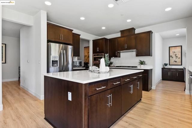 Kitchen featuring appliances with stainless steel finishes, recessed lighting, a center island, dark brown cabinets, and light wood finished floors
