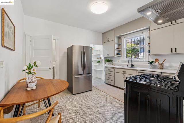 Kitchen with black range with gas stovetop, ventilation hood, open shelves, freestanding refrigerator, and light countertops