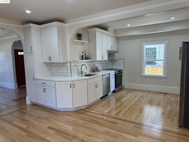 Kitchen with open shelves, arched walkways, backsplash, light countertops, and white cabinets