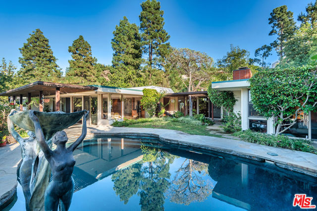Don't miss this wonderful opportunity to re-imagine this Mid Century located in prestigious Trousdale Estates. Set back from the street with just under 21,000sf of land sits this 4bed + 5 bath. Formal entry with marble floors leads to oversized stepdown living room with fireplace and floor-to-ceiling windows overlooking the pool with fountains. Formal dining adjacent to covered side patio with built-in BBQ, large kitchen with top of the line appliances, walk-in pantry and full breakfast room.  An abundance of natural light and recessed lighting throughout. Primary suite with stone fireplace, office/library and sumptuous bath with dual sinks, steam shower, and unique stepdown soaking tub.  Lush yard with mature trees overlook canyon views and pool. 3 car garage and 4 car driveway.