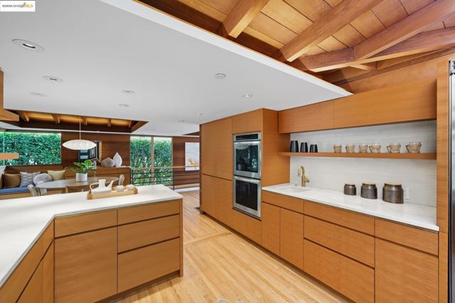 Kitchen featuring modern cabinets, light wood-type flooring, open shelves, double oven, and beamed ceiling