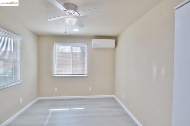 Empty room featuring a wall unit AC, ceiling fan, and light wood-style flooring