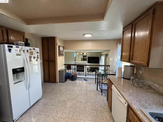 Kitchen with white appliances, brown cabinets, light stone counters, a textured ceiling, and light flooring
