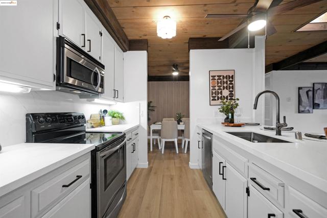 Kitchen featuring stainless steel appliances, white cabinets, ceiling fan, light stone countertops, and wooden ceiling