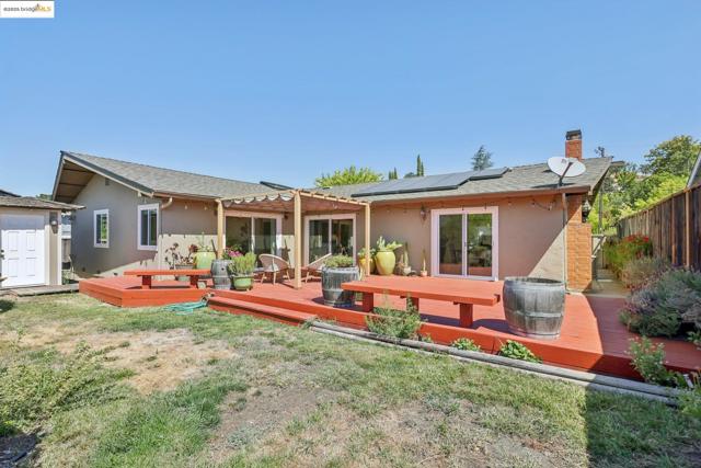 Rear view of property with stucco siding, a pergola, a chimney, roof mounted solar panels, and a deck