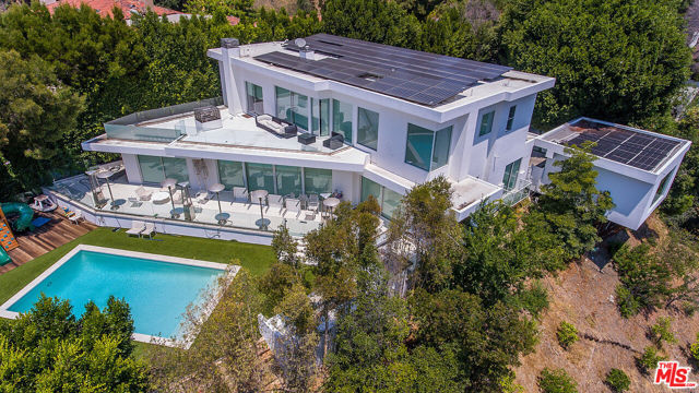 1247 LAGO VISTA Drive Beverly Hills, California Step into the most fabulous private Contemporary estate available in Beverly Hills! Stunning and Modern with breathtaking City-to-Ocean views from every room! Situated on a One acre street-to-street lot, this 4 BR & 5 BA home has it all. Arrive at stainless steel gates to a large tree-lined rare motor court with parking for 10-12 cars. Enter thru automatic glass doors into a home bathed in natural light with elegant proportions, dramatic height and walls of glass. The open floorplan features a living room with fireplace, dining area with fireplace, top-of-the-line center island kitchen which all open with motorized Fleetwood doors to a grand back patio, saltwater pool, fire pit, heat lamps, perfect for entertaining. Walking paths to fruit orchards and lush grounds with an abundance of mature avocado/lime/lemon/orange trees. The home features solar electric and pool heater making electricity practically free. Upstairs is an enormous luxurious primary suite with fireplace, private balcony, walk-in closets, spa-like bathroom. Views from this room are from downtown to Catalina Island and Long Beach. A second BR suite completes this floor. Downstairs is maids/guest suite with private entrance and a large family/media room with its own bathroom and fireplace. Seller is offering a credit with BAM Luxury Audio Video Cinema to refresh the Creston/Lutron system. This sophisticated home is nestled in a celebrity studded area with the ultimate in privacy and luxury. The adjacent home is on the market for $74M.