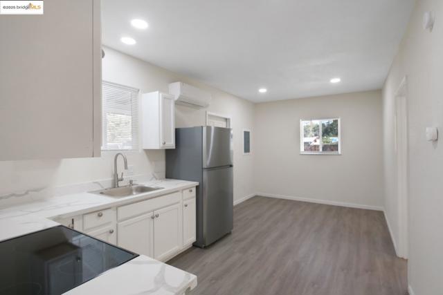 Kitchen featuring light wood finished floors, white cabinets, freestanding refrigerator, recessed lighting, and a wall mounted air conditioner