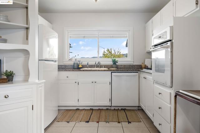 Kitchen featuring white cabinets, open shelves, white appliances, light tile patterned flooring, and dark stone counters