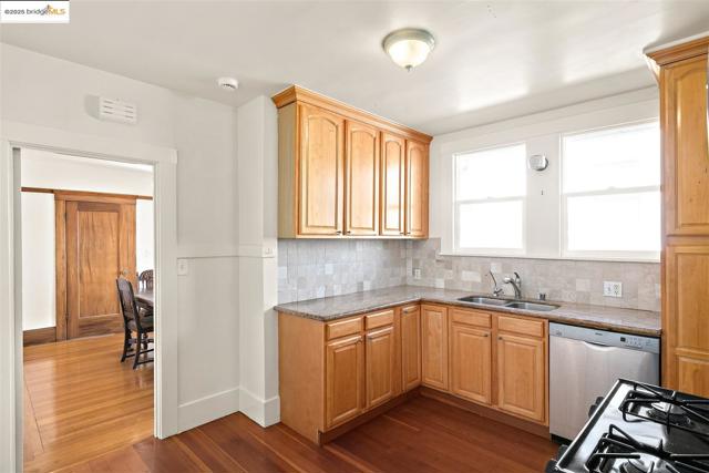 Kitchen with stainless steel dishwasher, dark wood-style flooring, light stone counters, decorative backsplash, and black gas stove