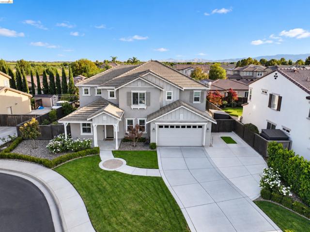 Two-story residence featuring a gray exterior with white trim, a covered entry porch, a two-car garage, an expansive concrete driveway, and a manicured lawn