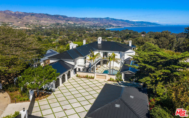 Gracious space, exquisite materials, and a lovely setting combine to create an atmosphere of elegance in this majestic Malibu estate. Built on a palatial scale, with soaring ceilings, stunning woodwork, and bespoke fixtures, the residence has been entirely remodeled inside and out with impeccable attention to detail. Every amenity of comfort and style is here, from the water features, swimming pool, and putting green to the library, gym, movie theater, and stunning bedroom suites. The gated entry opens to reveal a huge motor court flanked by a two-car garage on one side and a three-car garage on the other. Beyond a low wall, a long, covered walkway leads past the beautiful pool, infinity-edge Jacuzzi, and sun deck to the front door. Inside, the two-story foyer and the wide staircase is partially paneled with glossy blond wood, while the formal living room offers an ocean view just steps ahead. Hardwood floors, built-in cabinets, a wide fireplace, and a window-lined tower for the piano make a perfect setting for elegant entertaining. Two steps up is the formal dining room, with glass doors that open onto the ocean view patio. The professional chef's kitchen has handsome wood cabinets, a large island with bar seating, top-quality appliances, a butler's pantry, a wall of glass-front storage cabinets, a desk space, a sitting area with a fireplace, and a breakfast area in an ocean-view solarium. Doors open to an enormous, partially covered deck overlooking the backyard and ocean, with ample room for outdoor dining and lounging. Off the kitchen is an indoor entertainer's lounge complete with Caliber barbecue and smoker, fireplace, dining area, double sided aquarium, wet bar, media center, and a large, comfortable sitting area. Wide sliding glass doors open to the pool deck, where there are additional dining and seating areas. From the main hallway, dual glass doors in an arched doorway open to a spacious office with a marble fireplace, built-in library shelves, and views of the pool. Also on the main level is a powder room and a wine storage room. The home's lower floor comprises a stately movie theater, a large mirrored gym, a bathroom, and a bank-style vault room, as well as a laundry room and a bedroom suite with a kitchen. On the upper floor, a Juliet overlook opens to the foyer below, and a large living room/entertainment room provides additional shelf space, fireplace, seating, and glass doors to the ocean-view balcony. There are five bedrooms on this level, including the breathtaking primary suite, which has stunning woodwork, a fireplace with a sitting area, a service bar, a spectacular walk-in closet, a luxurious bath, and French doors to the view balcony. There is also a second laundry closet on this level. Off the back deck, the ocean-view back yard features an outdoor kitchen, a lounging space with a fire pit, and a large putting green. This is a home for sophisticated entertaining and a lifestyle of elegant comfort.