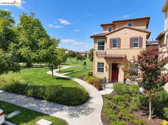 Stucco exterior with terracotta roof tiles, red entry door, decorative shutters, and established front landscaping