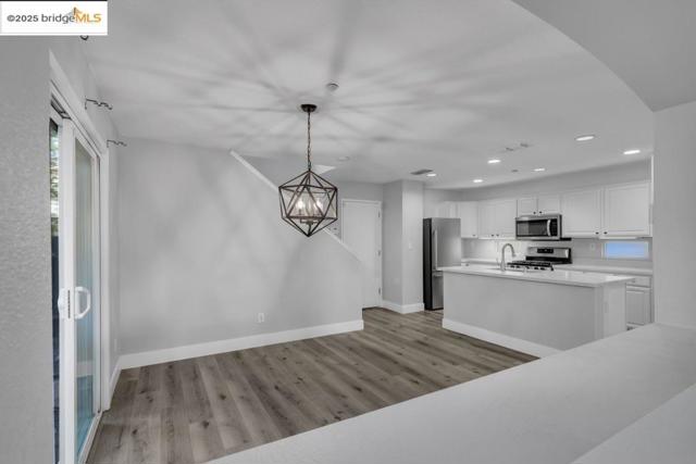 Kitchen with wood finished floors, a chandelier, appliances with stainless steel finishes, white cabinetry, and light countertops