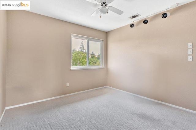 Carpeted empty room featuring a ceiling fan and track lighting