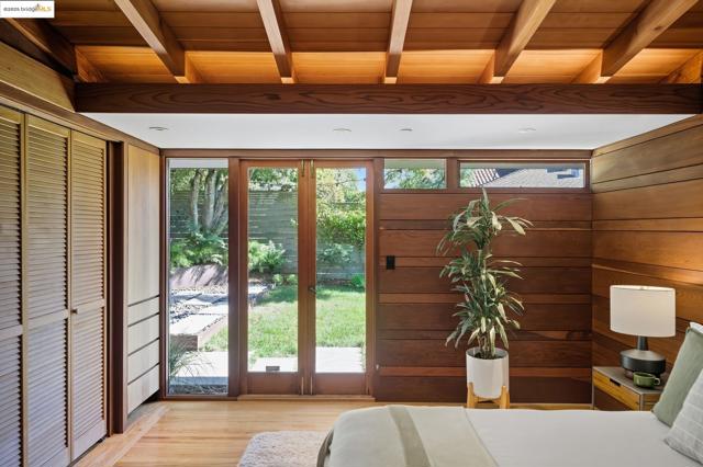 Bedroom with light wood-type flooring, wooden walls, a wood ceiling with exposed beams, access to outside, and a closet