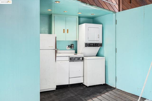 Kitchen with estacked washer and dryer, white appliances, dark wood-type flooring, light countertops, and white cabinets