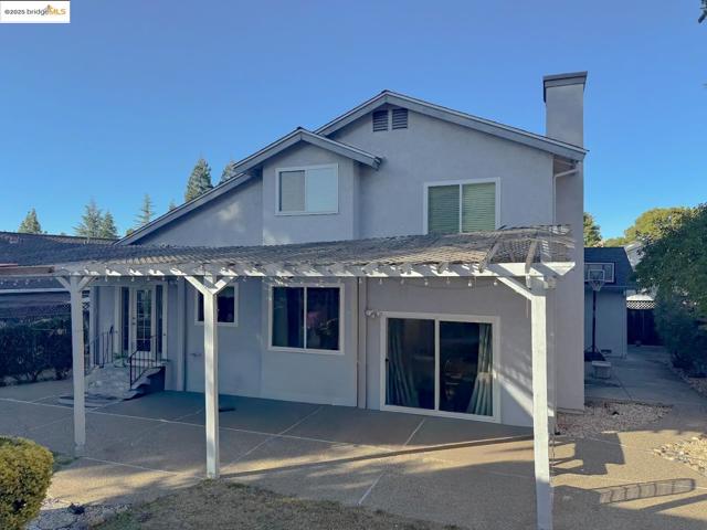 Rear view of house featuring a pergola, stucco siding, a chimney, and a patio