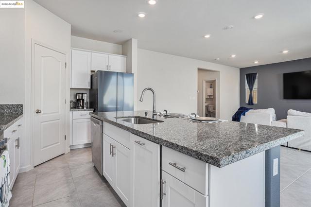 Kitchen featuring white cabinetry, stainless steel appliances, recessed lighting, dark stone counters, and a kitchen island with sink