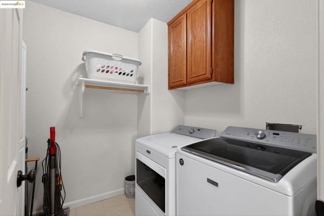 Laundry room with cabinet space, washing machine and dryer, light tile patterned floors, and a textured wall