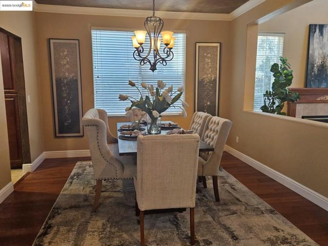 Dining area featuring ornamental molding, dark wood-style floors, a tiled fireplace, and a chandelier