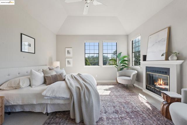 Carpeted bedroom featuring a ceiling fan, a glass covered fireplace, and lofted ceiling