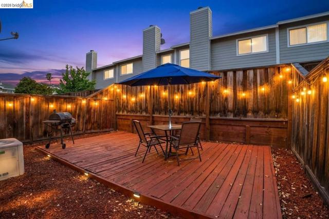 Fenced outdoor space featuring a wood deck, perimeter lighting, and bark ground cover. *Enhanced Evening Photo