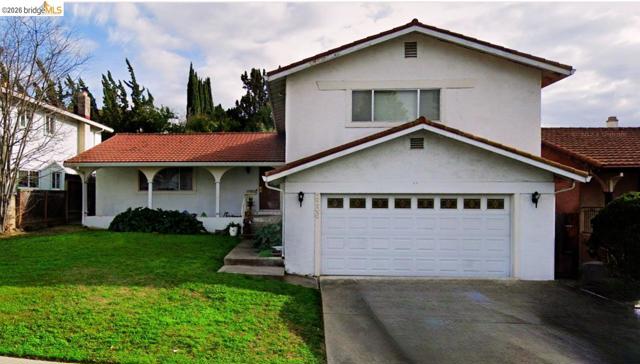 Stucco exterior with a terracotta tile roof, attached garage, and a covered porch with arched openings. The grass is no longer green.
