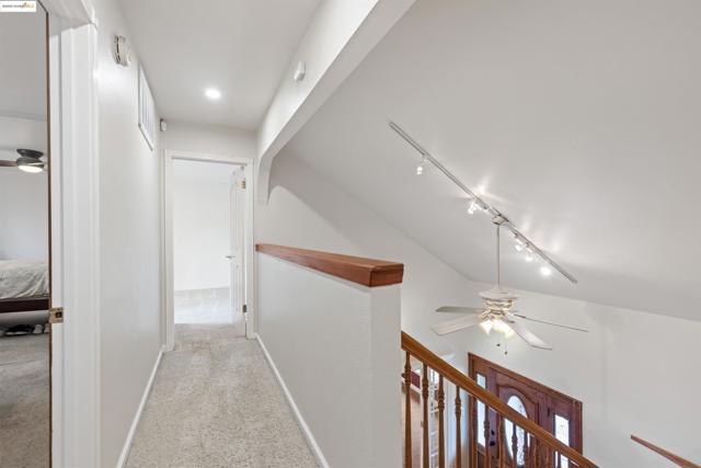 Hall with rail lighting, light colored carpet, and an upstairs landing