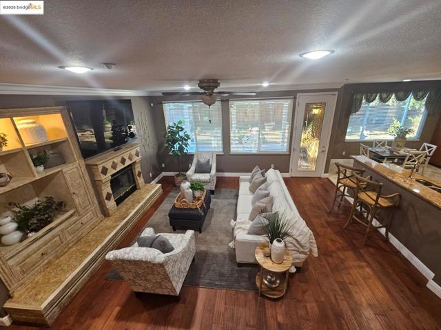 Living room featuring a textured ceiling, dark wood-style floors, a glass covered fireplace, healthy amount of natural light, and ceiling fan