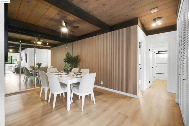 Dining room with a wooden ceiling with exposed beams, light wood finished floors, wood walls, and ceiling fan