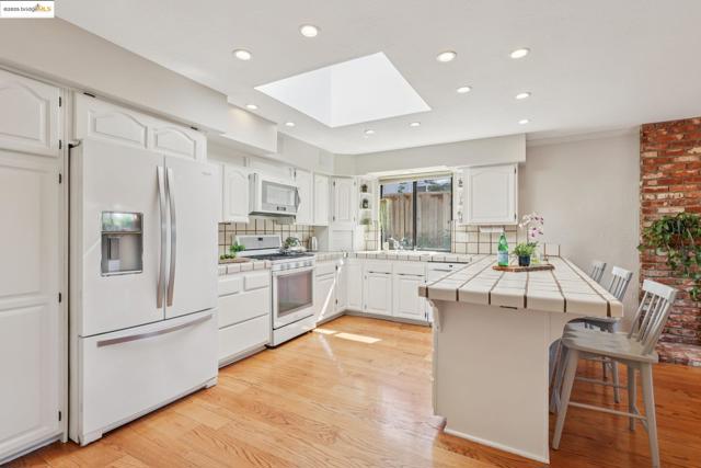 Kitchen featuring tile countertops, a skylight, white appliances, decorative backsplash, and recessed lighting