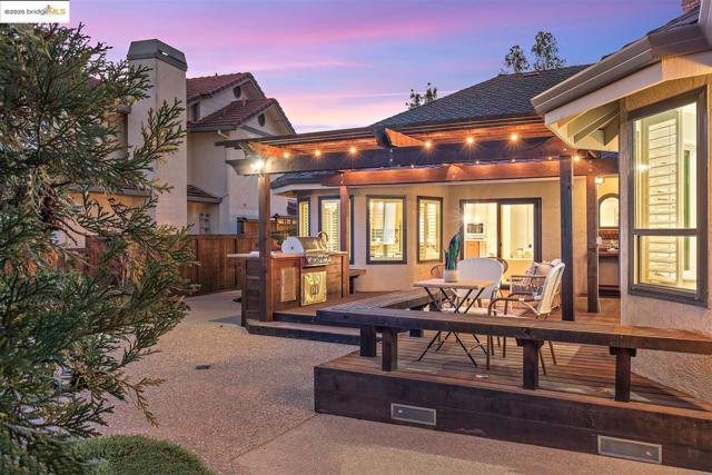 Back of property at dusk with an outdoor kitchen, outdoor dining space, stucco siding, and a chimney