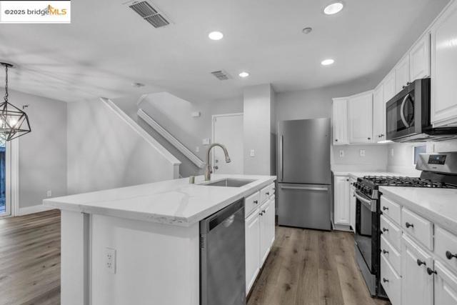 Kitchen featuring appliances with stainless steel finishes, a center island with sink, white cabinetry, wood finished floors, and recessed lighting