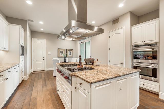 Gourmet kitchen with a spacious island, granite countertops, high-end appliances, and custom cabinetry. Open-concept design flows into the living area, perfect for entertaining. Warm wood flooring and a statement range hood add elegance and functionality.