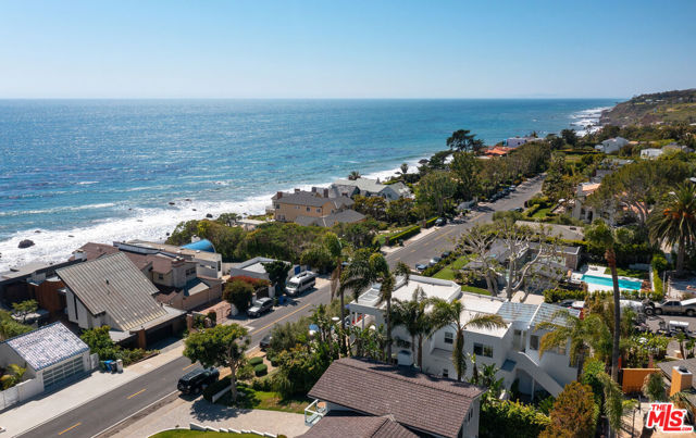 Open and comfortable, this Broad Beach contemporary occupies a gorgeously landscaped cul-de-sac corner lot with ocean views and across-the-street access to Sea Level Beach. With private patios and wraparound ocean-view decks, the home is both a private refuge and a lovely setting for indoor-outdoor entertaining. The living room is both spacious and open, with a fireplace, an enormous picture window onto a palm-fringed garden, and sliding glass doors to an outdoor living and dining patio. A wide doorway opens into the kitchen/dining room, complete with island, bar seating, top-grade appliances, and another glass door to the backyard. Just outside, the ocean-view flagstone patio features a fire pit with ample seating, a table for al fresco dining, and a built-in culinary center with a grill and sink. Also on the home's first level are a butler's pantry and two bedrooms. Sliding glass doors open onto an enclosed side yard with a large Jacuzzi and an outdoor shower. Beyond that, another door leads to a private patio area with additional room for relaxing and dining, plus a second outdoor shower. There are three additional ocean-view bedrooms upstairs, including the tranquil primary suite, which has a wraparound, tiled deck with panoramic views and an infrared sauna, as well as dual closets and a luxurious bath. The home has a two-car garage and guest parking, plus another beach-like outdoor recreation area to the side of the main entry. This lovely property combines the quiet comfort of Western Malibu and all the attractions of the beach lifestyle.