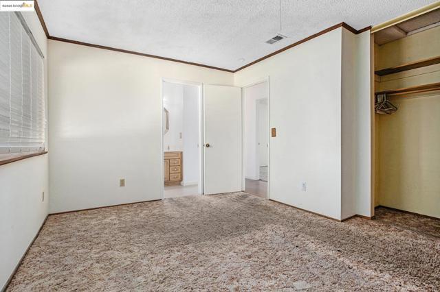 Unfurnished bedroom with crown molding, carpet flooring, a textured ceiling, a closet, and ensuite bath