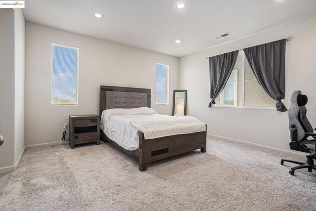 Bedroom with light colored carpet, recessed lighting, and a desk