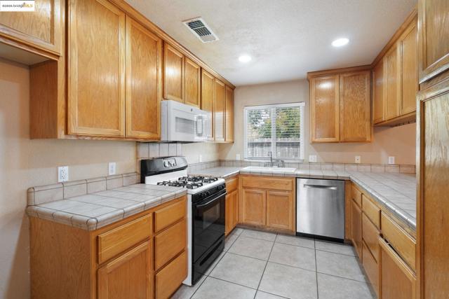 Kitchen featuring gas stove, tile counters, dishwasher, light tile patterned flooring, and white microwave