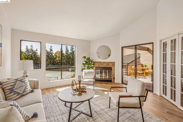 Living area featuring vaulted ceilings, wood-finish flooring, a tile-surround fireplace, large windows, and a sliding glass door providing external access
