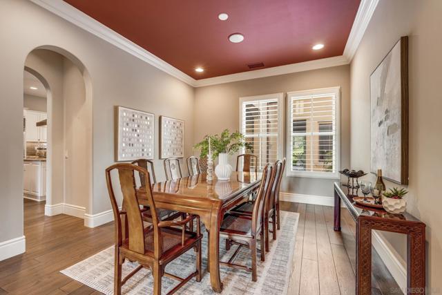 Elegant Dining Room with rich wood flooring, a striking statement ceiling, and large windows with plantation shutters that invite natural light. The space seamlessly connects to the kitchen, creating an ideal setting for gatherings.