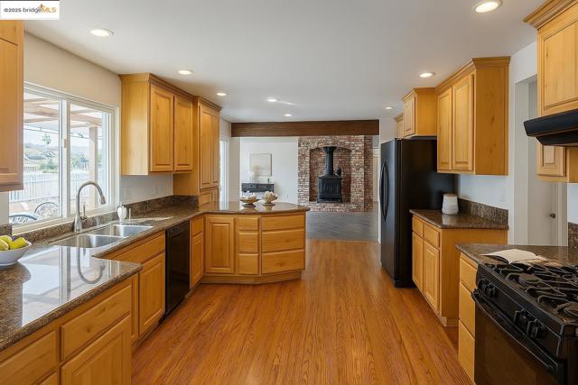 Kitchen featuring a wood stove, dark stone counters, light wood-style flooring, recessed lighting, and black appliances
