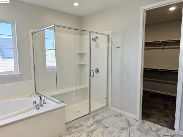 Bathroom featuring a shower stall, a walk in closet, a garden tub, light marble finish flooring, and recessed lighting