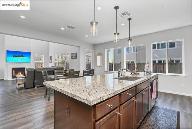 Kitchen featuring a warm lit fireplace, hanging light fixtures, light stone countertops, open floor plan, and recessed lighting