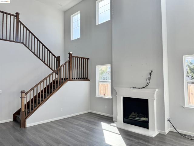 Unfurnished living room with a high ceiling, wood finished floors, a fireplace with raised hearth, and stairs