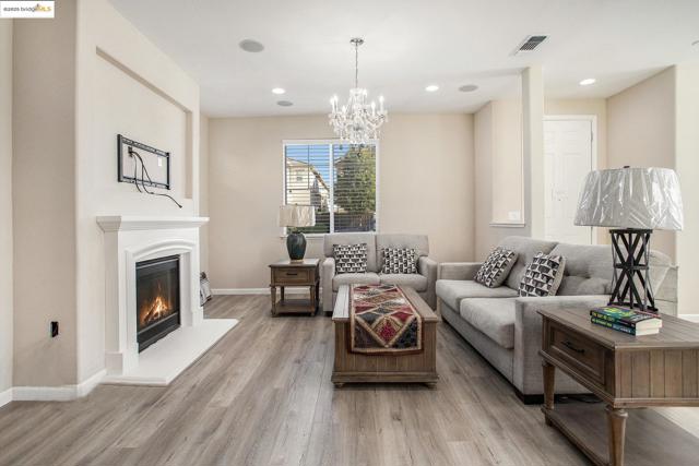 Living room with light wood-style floors, a glass covered fireplace, a chandelier, and recessed lighting
