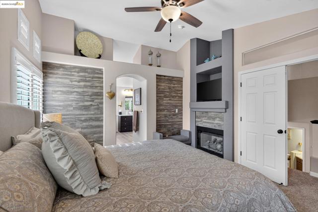 Carpeted bedroom with ensuite bath, arched walkways, a glass covered fireplace, and a ceiling fan